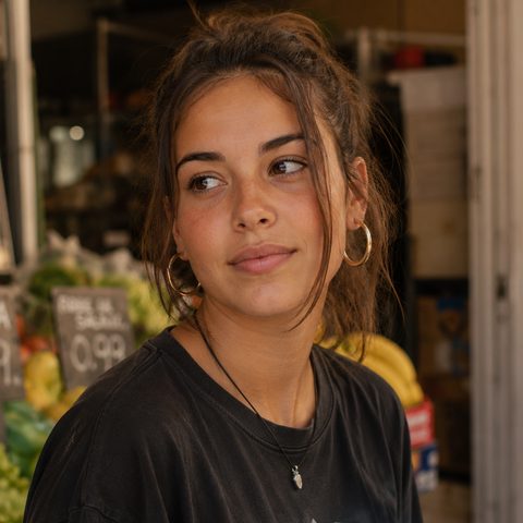 Mujer joven con el móvil en la mano, en la puerta de un puesto del mercado