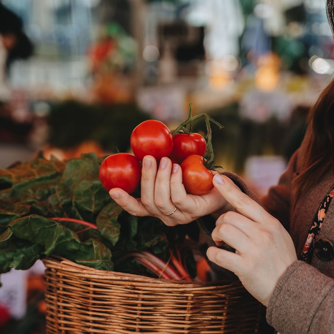 Una clienta con cesta de mimbre elige tomates en el puesto de frutas y verduras