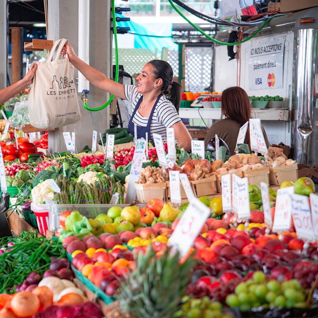 La tendera entrega la bolsa de la compra a una clienta sobre el mostrador de verduras